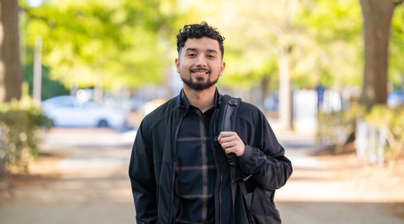 A student stands on campus with their backpack slung across their shoulder. 